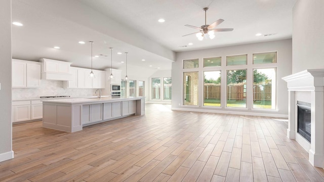 kitchen with pendant lighting, a center island with sink, sink, light wood-type flooring, and white cabinetry