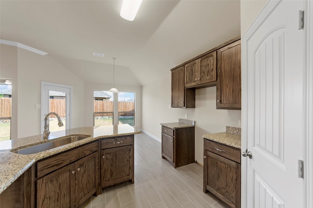 kitchen featuring light stone countertops, sink, decorative light fixtures, and vaulted ceiling