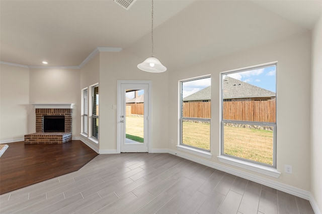 unfurnished living room featuring vaulted ceiling, crown molding, hardwood / wood-style floors, and a brick fireplace