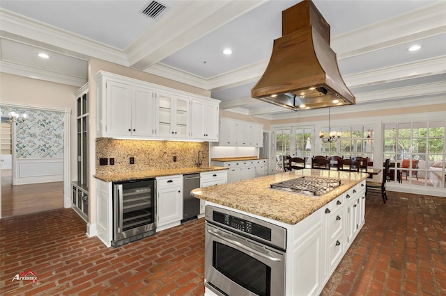 kitchen with beverage cooler, island exhaust hood, stainless steel appliances, light stone counters, and white cabinetry