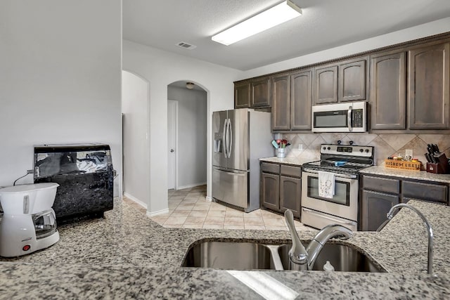 kitchen with light tile floors, appliances with stainless steel finishes, tasteful backsplash, and light stone countertops