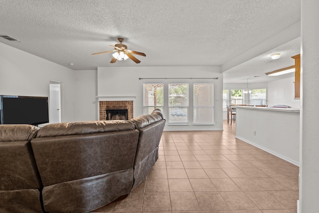 living room featuring ceiling fan, light tile patterned flooring, a textured ceiling, and a brick fireplace