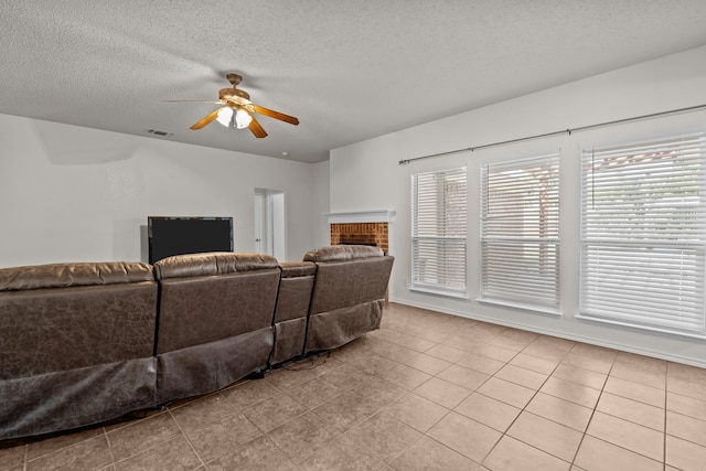 tiled living room featuring ceiling fan, a fireplace, and a textured ceiling