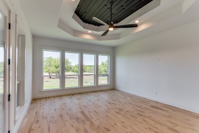 empty room with light hardwood / wood-style flooring, a tray ceiling, and ceiling fan