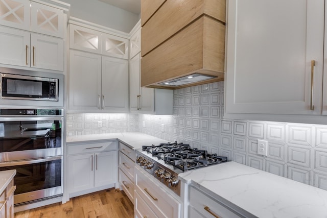 kitchen with premium range hood, stainless steel appliances, light wood-type flooring, and white cabinetry