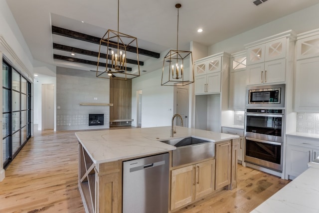 kitchen featuring beamed ceiling, sink, a center island with sink, appliances with stainless steel finishes, and a notable chandelier