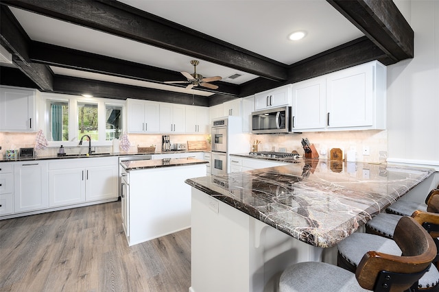 kitchen with ceiling fan, stainless steel appliances, white cabinets, beamed ceiling, and hardwood / wood-style floors