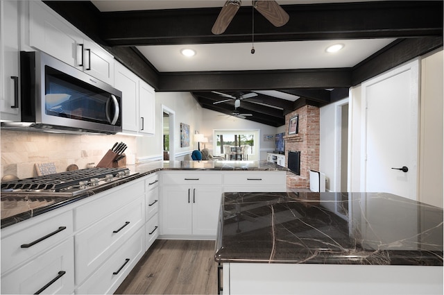 living room featuring ceiling fan, vaulted ceiling with beams, brick wall, a fireplace, and light wood-type flooring