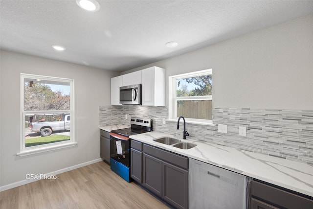 kitchen featuring sink, stainless steel appliances, light stone countertops, white cabinetry, and light wood-type flooring