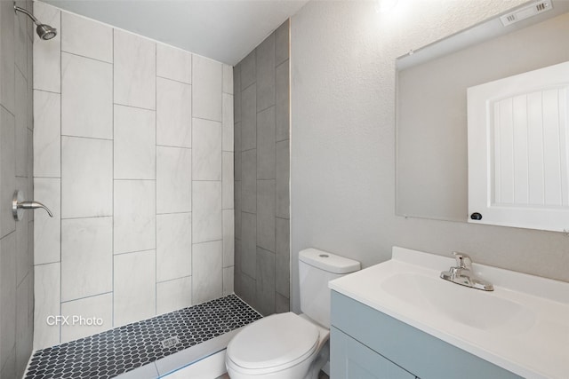 bathroom with toilet, a tile shower, and vanity