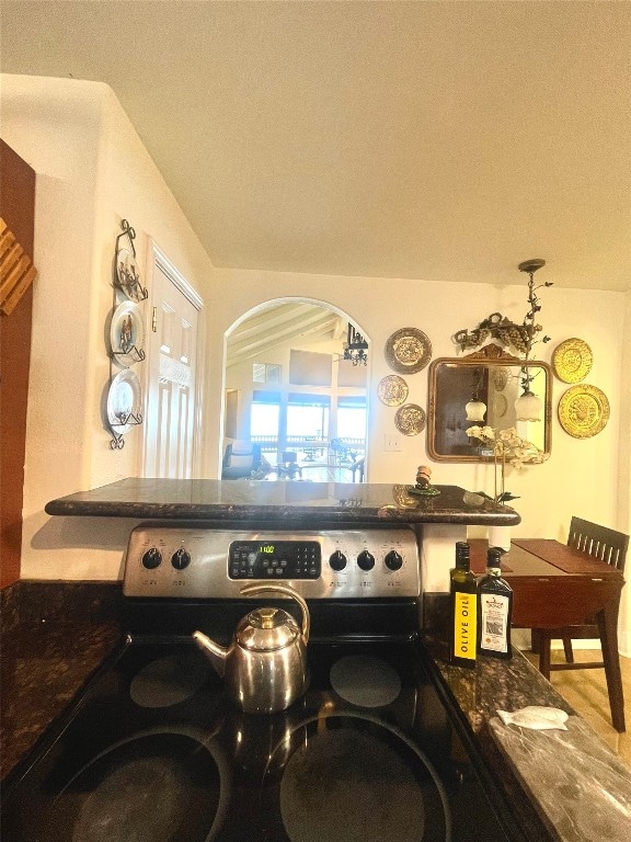 interior space featuring stainless steel electric range, hardwood / wood-style floors, dark stone countertops, and a chandelier