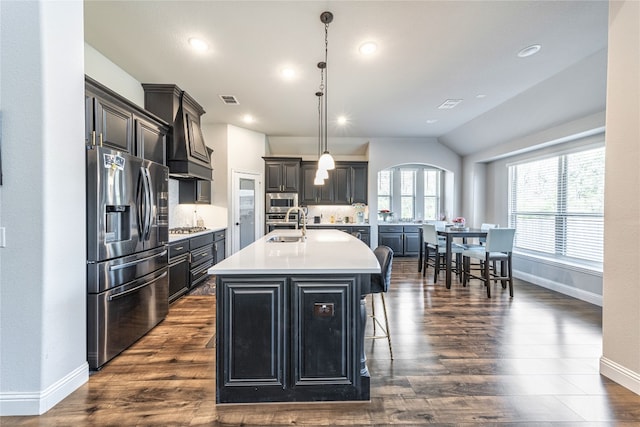 kitchen featuring appliances with stainless steel finishes, pendant lighting, dark wood-type flooring, and a kitchen island with sink