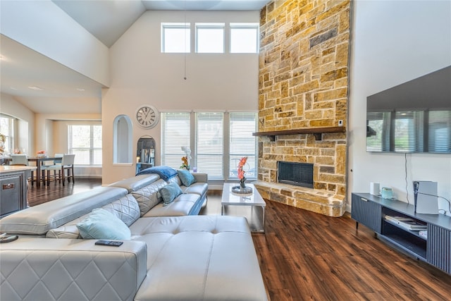 living room featuring high vaulted ceiling, a stone fireplace, and dark wood-type flooring