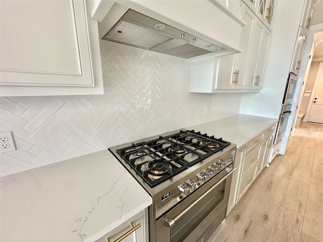 kitchen with premium range hood, stainless steel gas range oven, white cabinetry, light hardwood / wood-style flooring, and light stone countertops