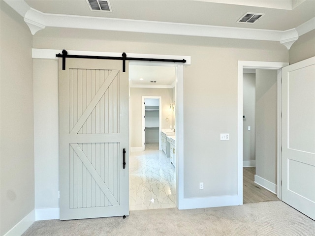 unfurnished bedroom featuring light carpet, a spacious closet, ornamental molding, and a barn door