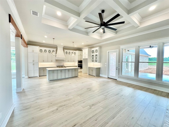 interior space featuring pendant lighting, a center island with sink, custom range hood, a healthy amount of sunlight, and white cabinets