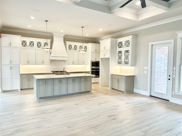 kitchen featuring appliances with stainless steel finishes, hanging light fixtures, custom range hood, and a center island with sink