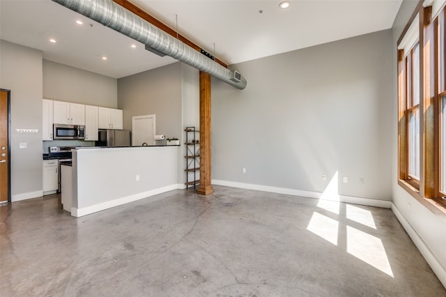 kitchen featuring appliances with stainless steel finishes, a kitchen island, concrete flooring, a towering ceiling, and white cabinets