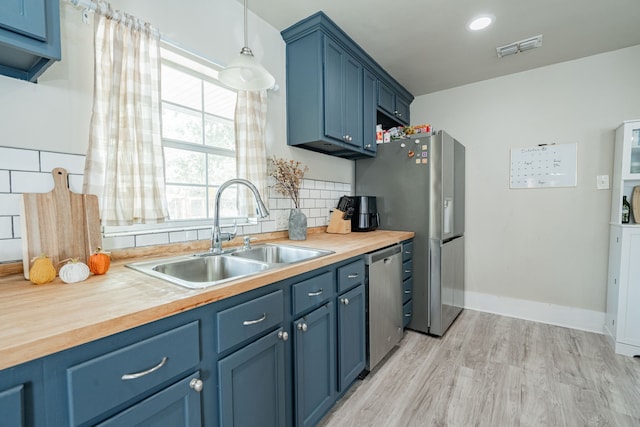 kitchen featuring sink, butcher block counters, backsplash, blue cabinets, and stainless steel appliances