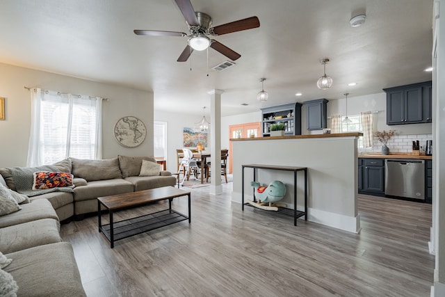 living room featuring decorative columns, ceiling fan with notable chandelier, and light hardwood / wood-style floors