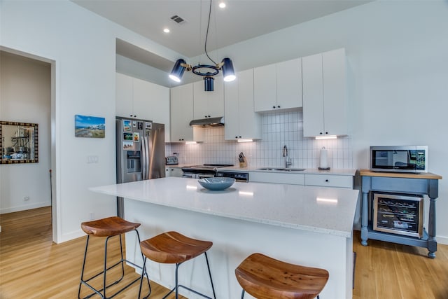 kitchen featuring under cabinet range hood, stainless steel appliances, a breakfast bar, a sink, and visible vents