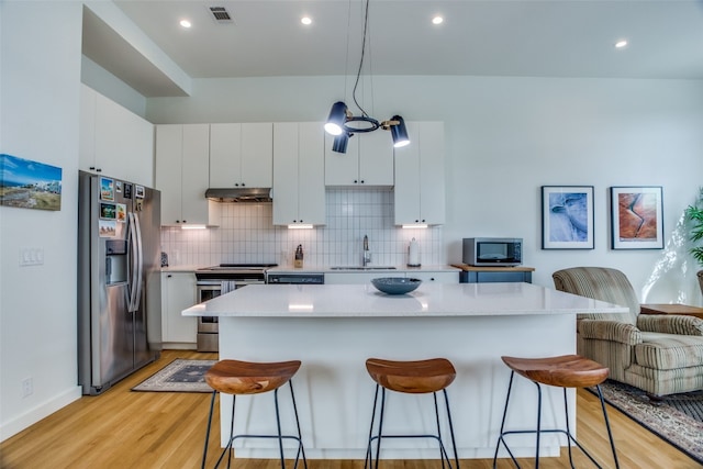 kitchen with a breakfast bar area, stainless steel appliances, backsplash, a sink, and under cabinet range hood