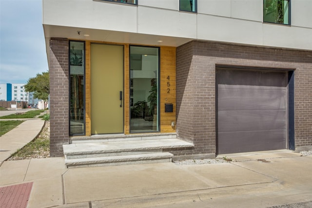 view of exterior entry featuring a garage and brick siding