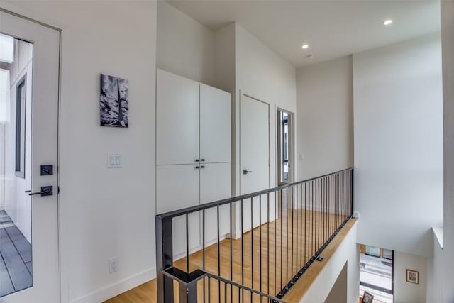 corridor with recessed lighting, baseboards, wood finished floors, and an upstairs landing