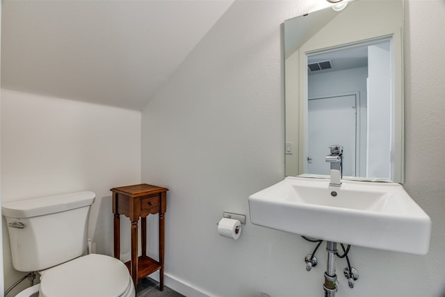 bathroom featuring baseboards, visible vents, toilet, vaulted ceiling, and a sink