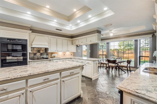 kitchen with custom exhaust hood, black appliances, a raised ceiling, decorative backsplash, and ornamental molding