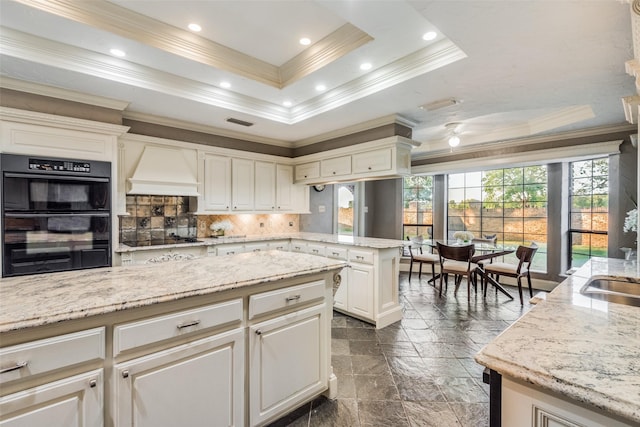 kitchen featuring custom exhaust hood, stone tile flooring, a raised ceiling, a peninsula, and black appliances