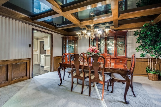 carpeted dining room featuring wallpapered walls, coffered ceiling, ornamental molding, an inviting chandelier, and beam ceiling