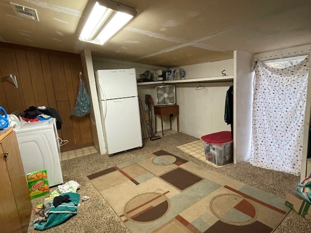 basement featuring wooden walls, washer / clothes dryer, and white refrigerator