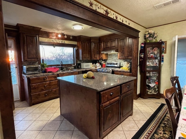 kitchen featuring stainless steel gas range, sink, dark stone counters, a textured ceiling, and a kitchen island