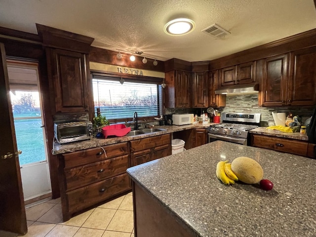 kitchen with stainless steel gas range oven, a textured ceiling, light tile floors, and dark stone countertops