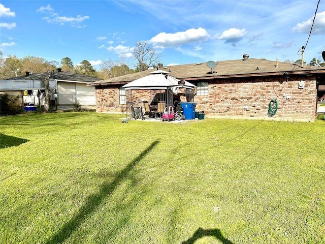 back of property featuring a gazebo, brick siding, and a lawn