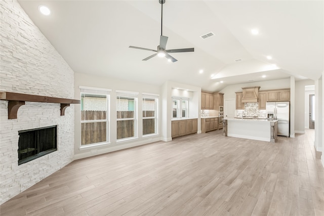 unfurnished living room featuring ceiling fan, high vaulted ceiling, light hardwood / wood-style flooring, and a stone fireplace