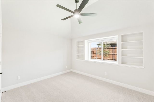 empty room with carpet floors, vaulted ceiling, ceiling fan, and built in shelves