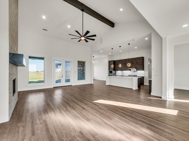 unfurnished living room with high vaulted ceiling, beamed ceiling, a large fireplace, dark wood-type flooring, and french doors