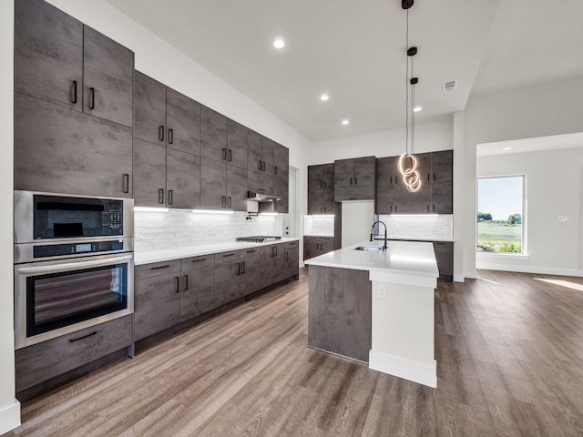 kitchen with appliances with stainless steel finishes, decorative light fixtures, sink, and light wood-type flooring