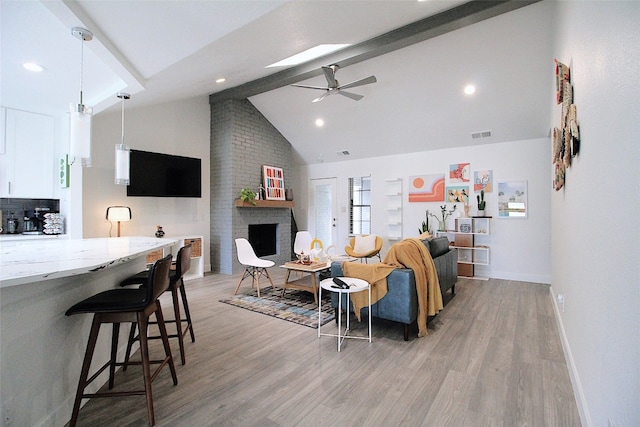 living room with light hardwood / wood-style floors, brick wall, a brick fireplace, ceiling fan, and lofted ceiling with beams