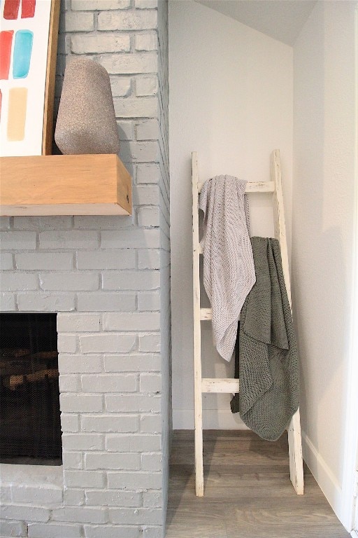 interior space featuring hardwood / wood-style floors, lofted ceiling, brick wall, and a brick fireplace