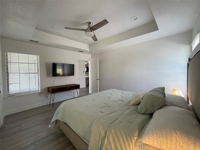 bedroom with ceiling fan, a textured ceiling, dark hardwood / wood-style floors, and a raised ceiling