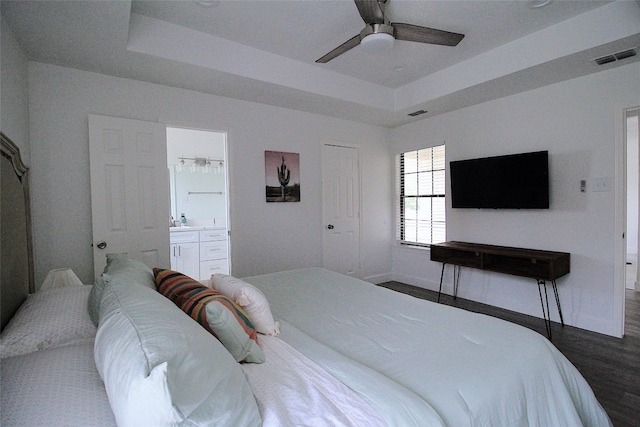 bedroom featuring ceiling fan, dark hardwood / wood-style floors, a tray ceiling, and ensuite bathroom