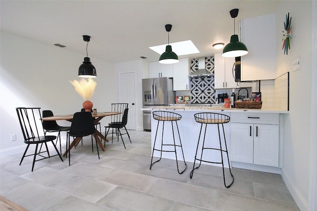 kitchen with backsplash, wall chimney exhaust hood, decorative light fixtures, and light tile floors