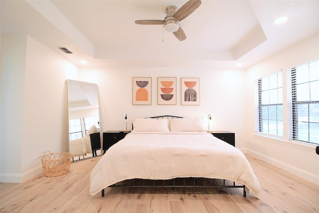 bedroom with light hardwood / wood-style floors, ceiling fan, and a tray ceiling