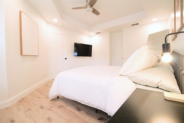 bedroom with light hardwood / wood-style floors, ceiling fan, and a tray ceiling