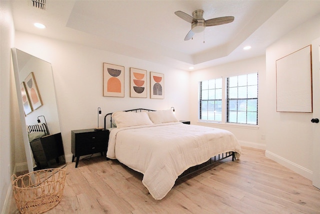 bedroom featuring ceiling fan, light hardwood / wood-style floors, and a raised ceiling