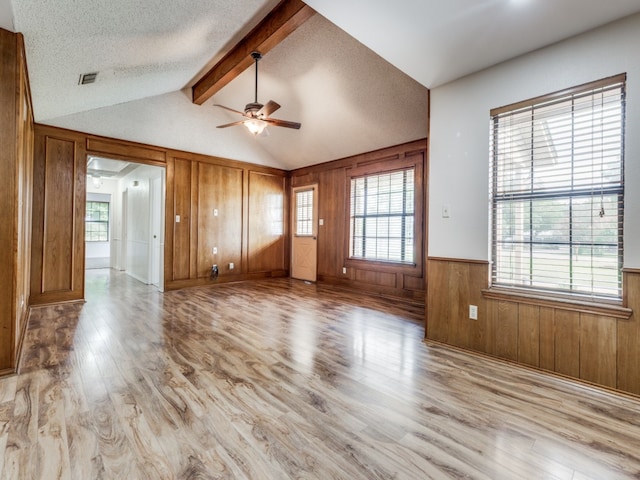 unfurnished living room featuring ceiling fan, vaulted ceiling with beams, a healthy amount of sunlight, and light hardwood / wood-style flooring