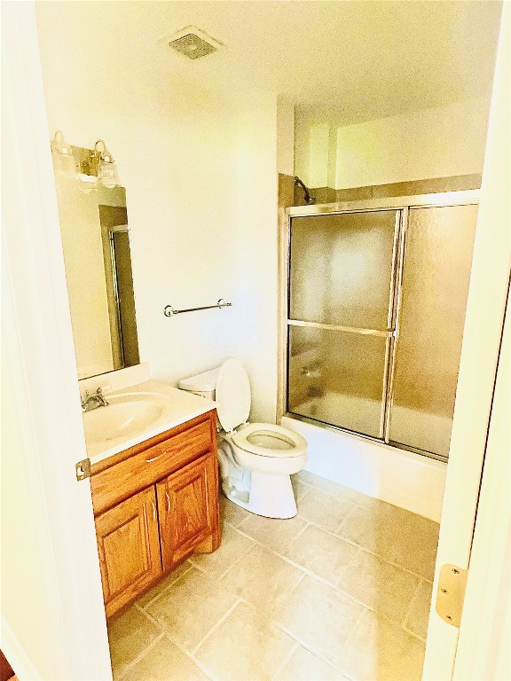 full bathroom with combined bath / shower with glass door, tile flooring, large vanity, and toilet